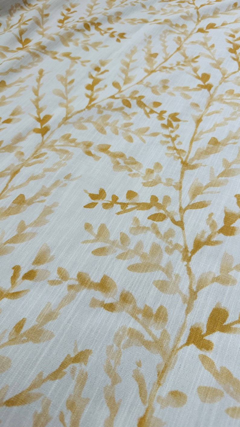 May include: White fabric with a subtle texture featuring a repeating pattern of gold-colored leafy branches.