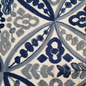 May include: A white fabric with blue and gray embroidered patterns. The design features intricate geometric shapes and floral motifs.