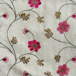 May include: A white fabric with a delicate embroidered floral pattern. The flowers are pink and the stems are brown.