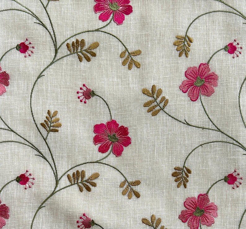May include: A white fabric with a delicate embroidered floral pattern. The flowers are pink and the stems are brown.
