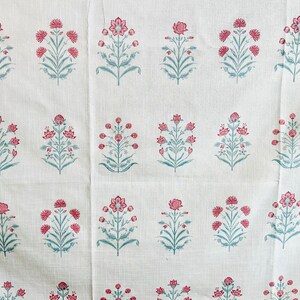 May include: White fabric with a repeating pattern of pink and blue floral designs. The fabric has a subtle texture.
