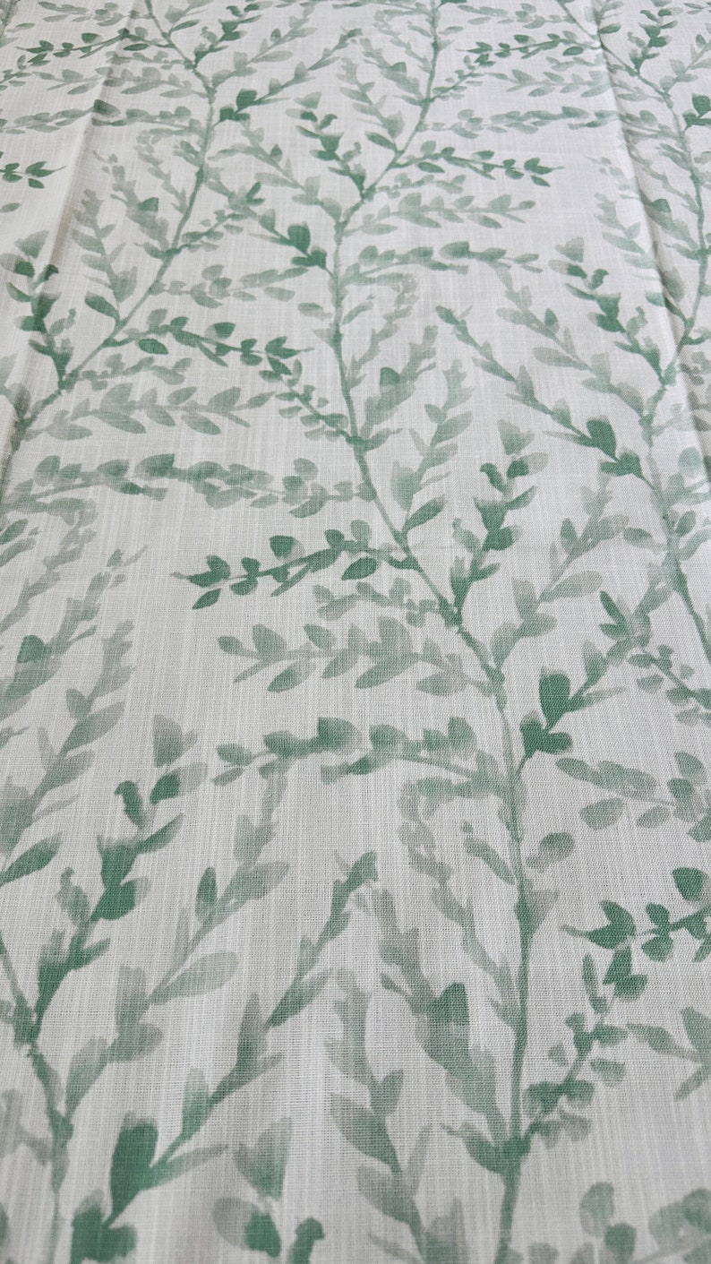 May include: A white fabric with a green leafy pattern. The leaves are painted in a watercolor style and are scattered across the fabric.