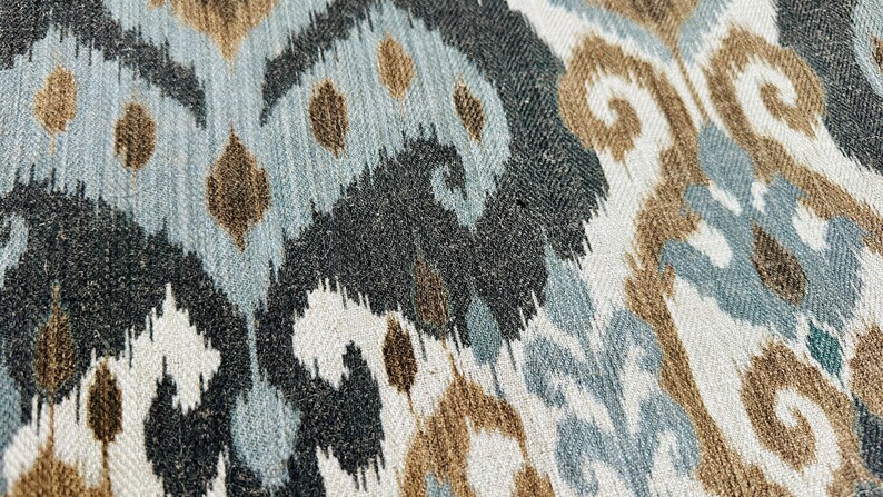 Puede incluir: Primer plano de una tela con un patr&oacute;n ikat marr&oacute;n, azul y blanco. La tela tiene una superficie texturizada y un aspecto tejido.