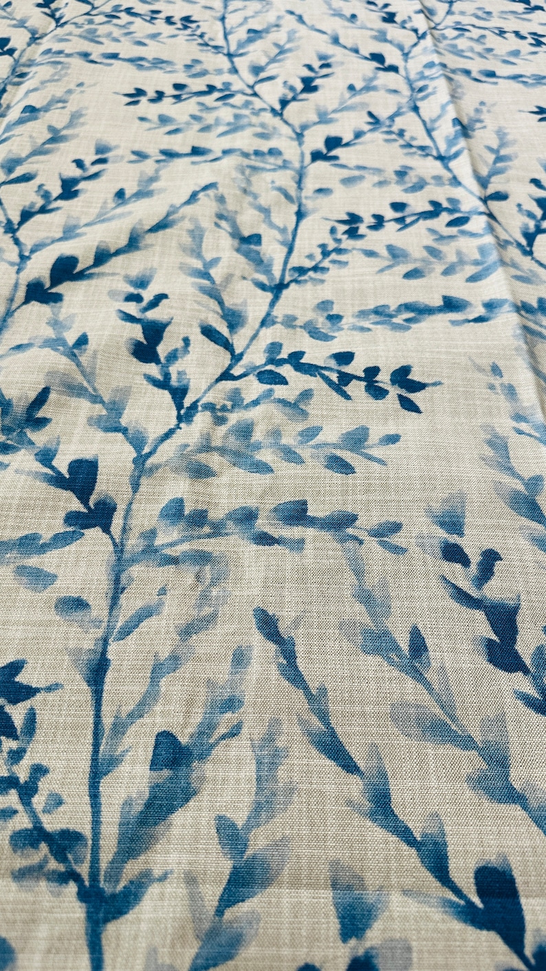 May include: Close-up of a fabric with a repeating pattern of blue watercolor-style branches and leaves against a neutral beige background. The fabric has a linen-like texture, creating a natural and organic feel. The design is suitable for home decor.