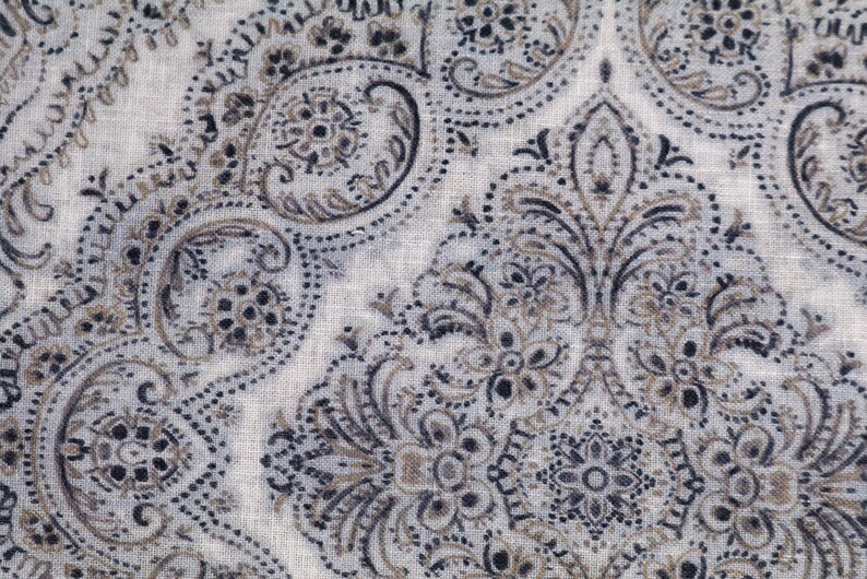May include: A white fabric with a paisley pattern in shades of brown and black. The fabric has a subtle texture and a delicate design.