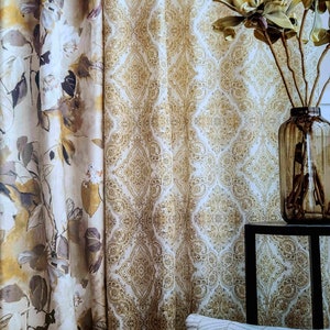 May include: Two patterned curtains, one with a floral design and the other with a paisley design, hang in a window. A vase with dried branches sits on a black table in front of the curtains.