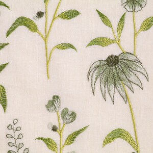 May include: A white fabric with an embroidered floral pattern. The flowers are green and white with a light brown center. The fabric has a subtle texture.