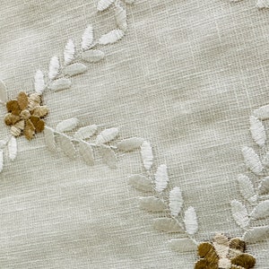 May include: White fabric with a delicate embroidered pattern of leaves and flowers. The leaves are white and the flowers are a light brown color.