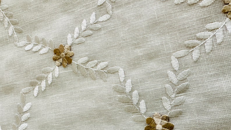 May include: White fabric with a delicate embroidered pattern of leaves and flowers. The leaves are white and the flowers are a light brown color.