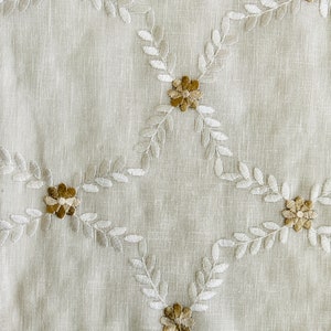 May include: White fabric with a delicate pattern of embroidered leaves and flowers in shades of beige and brown.