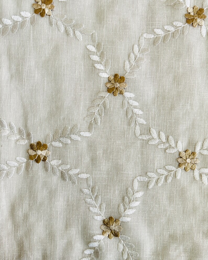 May include: White fabric with a delicate pattern of embroidered leaves and flowers in shades of beige and brown.