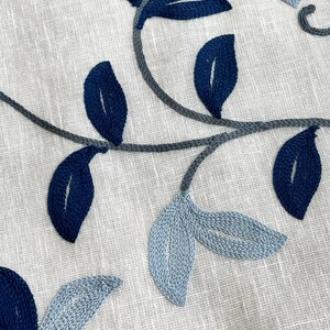 May include: A close-up of a white fabric with blue and gray embroidered leaves. The leaves are in a variety of shapes and sizes, and they are arranged in a flowing pattern.
