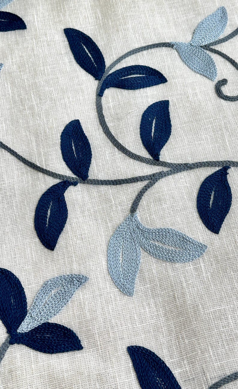 May include: A close-up of a white fabric with blue and gray embroidered leaves. The leaves are in a variety of shapes and sizes, and they are arranged in a flowing pattern.