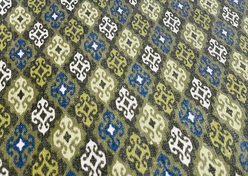 May include: A green, blue, and white fabric with a repeating geometric pattern. The pattern is made up of small squares with a stylized floral design in the center.