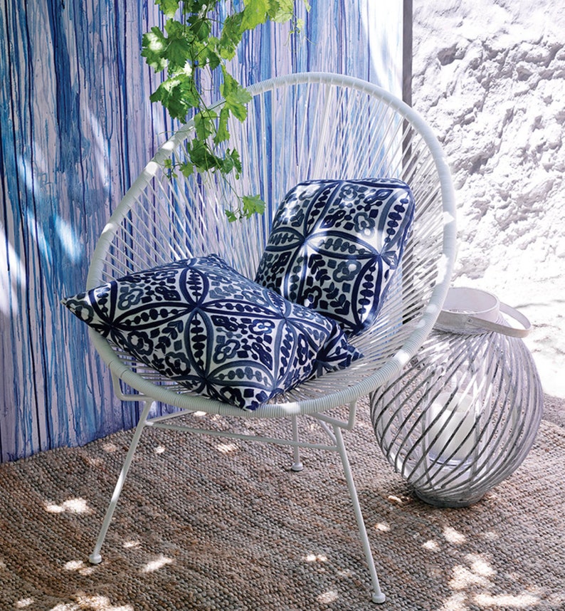 May include: White outdoor chair with a round back and two blue and white patterned pillows. The chair is sitting on a woven rug in front of a blue and white striped wall.
