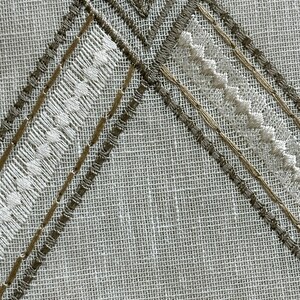May include: A white fabric with a brown and white embroidered design. The design features a diamond shape with a smaller square inside.