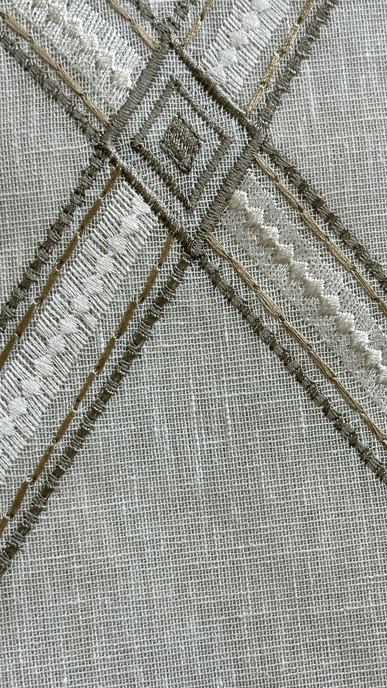 May include: A white fabric with a brown and white embroidered design. The design features a diamond shape with a smaller square inside.