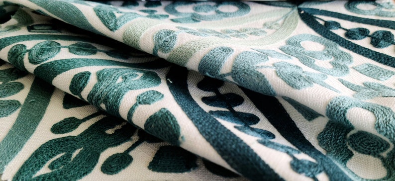 May include: White fabric with a teal blue embroidered floral pattern. The fabric is folded in half, showing the pattern on both sides.