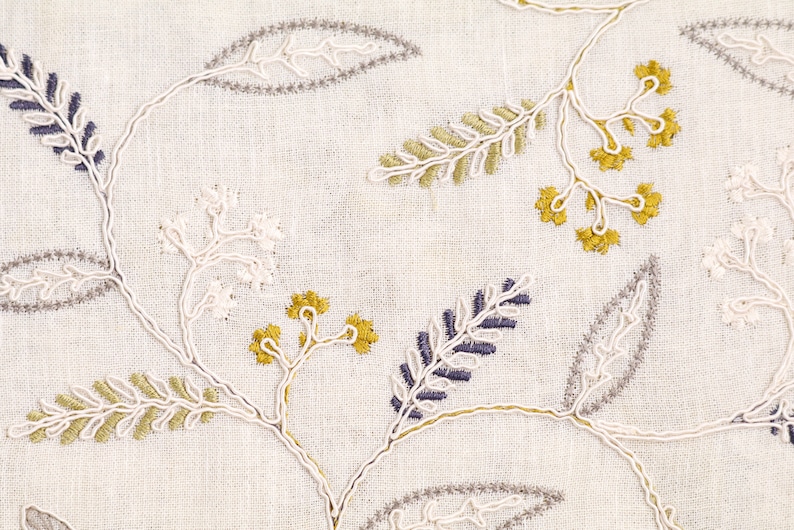 May include: White fabric with embroidered floral designs in shades of gray, white, yellow, and blue.