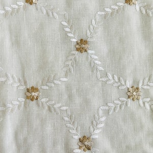 May include: White fabric with a delicate embroidered pattern of small flowers and leaves in a light brown color.