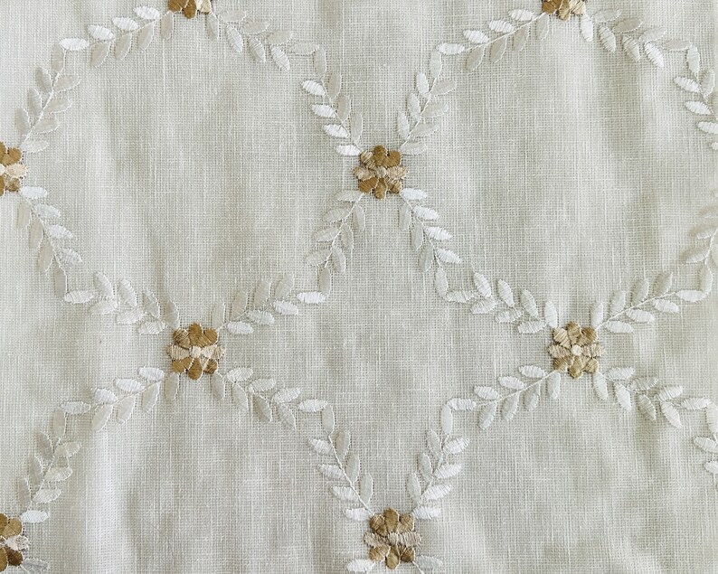 May include: White fabric with a delicate embroidered pattern of small flowers and leaves in a light brown color.
