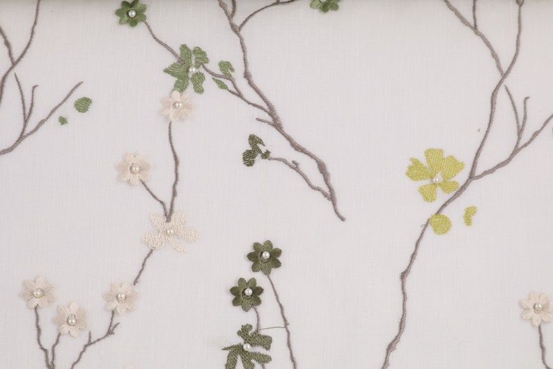 May include: White sheer fabric with embroidered floral designs in shades of green, beige, and yellow. The flowers have pearl accents.