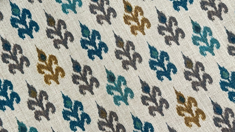 May include: A white fabric with a repeating pattern of stylized leaves in shades of teal, gray, and gold.
