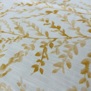 May include: White fabric with a subtle pattern of yellow leafy branches. The fabric has a soft, textured look.