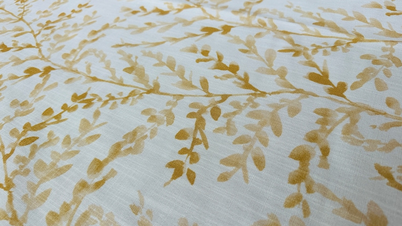 May include: White fabric with a subtle pattern of yellow leafy branches. The fabric has a soft, textured look.