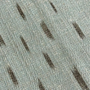 Puede incluir: Primer plano de una tela azul claro con un sutil patr&oacute;n de espiga y rayas gris oscuro.