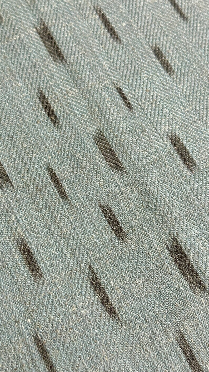 Puede incluir: Primer plano de una tela azul claro con un sutil patr&oacute;n de espiga y rayas gris oscuro.