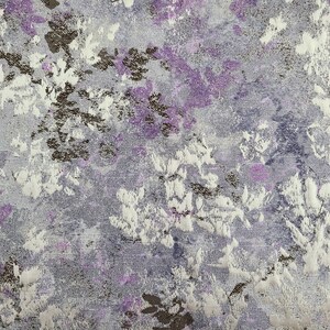 Pu&ograve; includere: Primo piano di un tessuto con un motivo floreale in tonalit&agrave; di viola, bianco e marrone. Il tessuto ha una superficie testurizzata e un leggero bagliore.