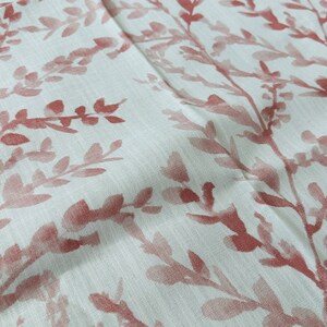 May include: A white fabric with a repeating pattern of pink floral sprigs. The fabric has a subtle texture.