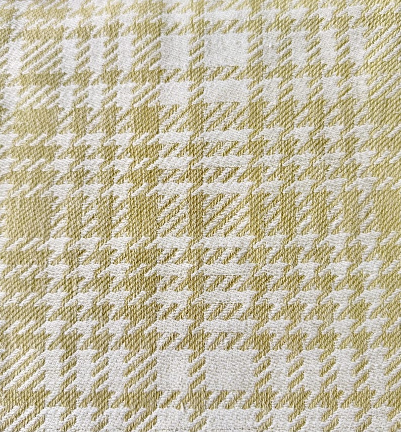 May include: A woven fabric featuring a repeating houndstooth pattern in shades of light olive green and off-white. The textile displays a dense, textured weave with a consistent grid-like structure throughout the entire surface area.