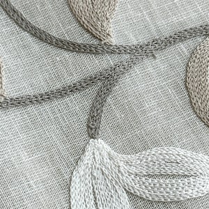 May include: Close-up of a white linen fabric with embroidered leaves in beige and white thread. The leaves are arranged in a flowing pattern.