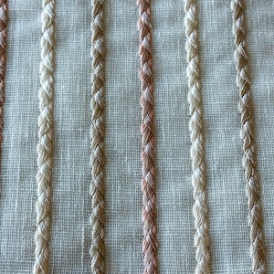 Puede incluir: Primer plano de una tela blanca con rayas verticales de hilo beige, marr&oacute;n y rosa. Las rayas est&aacute;n tejidas en la tela y crean un aspecto texturizado.