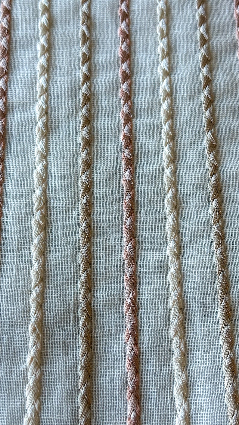 Puede incluir: Primer plano de una tela blanca con rayas verticales de hilo beige, marr&oacute;n y rosa. Las rayas est&aacute;n tejidas en la tela y crean un aspecto texturizado.