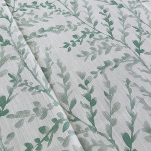 May include: A white fabric with a green leafy pattern. The fabric has a subtle texture and a light, airy feel.