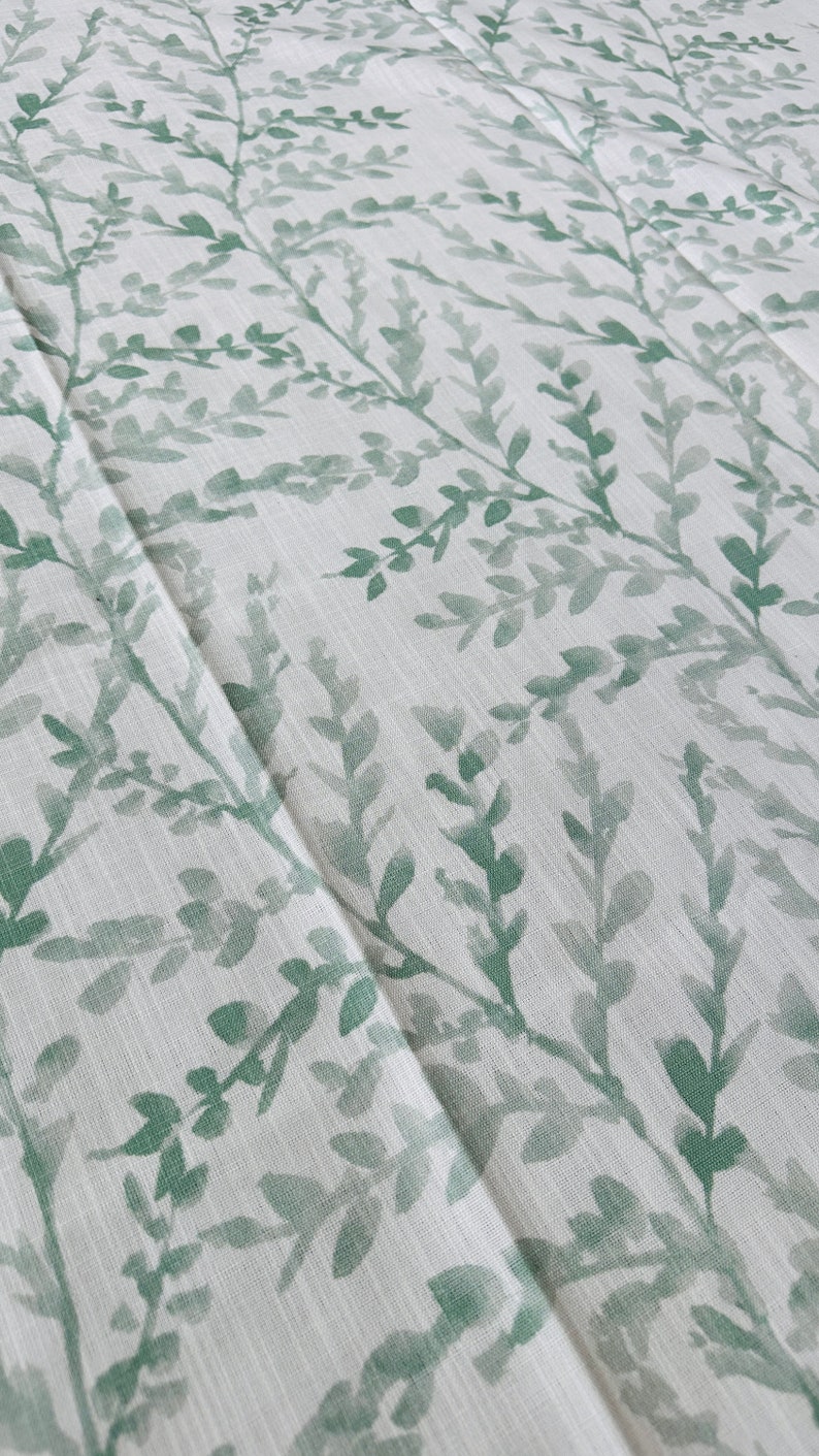 May include: A white fabric with a green leafy pattern. The fabric has a subtle texture and a light, airy feel.
