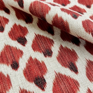 May include: Red and white fabric with a repeating pattern of red, black, and white ikat-style animal print.