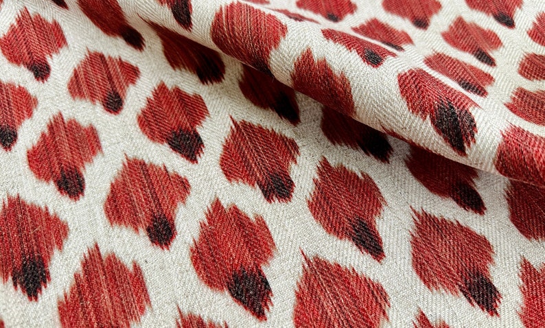 May include: Red and white fabric with a repeating pattern of red, black, and white ikat-style animal print.