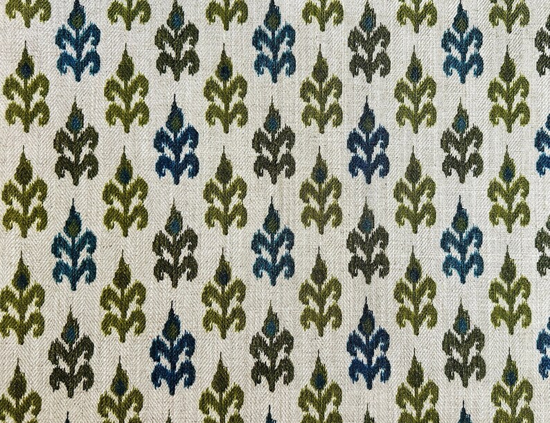 May include: A white fabric with a repeating pattern of green and blue stylized leaves. The fabric has a subtle herringbone weave.