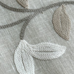 May include: Close-up of a beige fabric with white and brown embroidered leaves. The leaves are stitched in a detailed pattern.