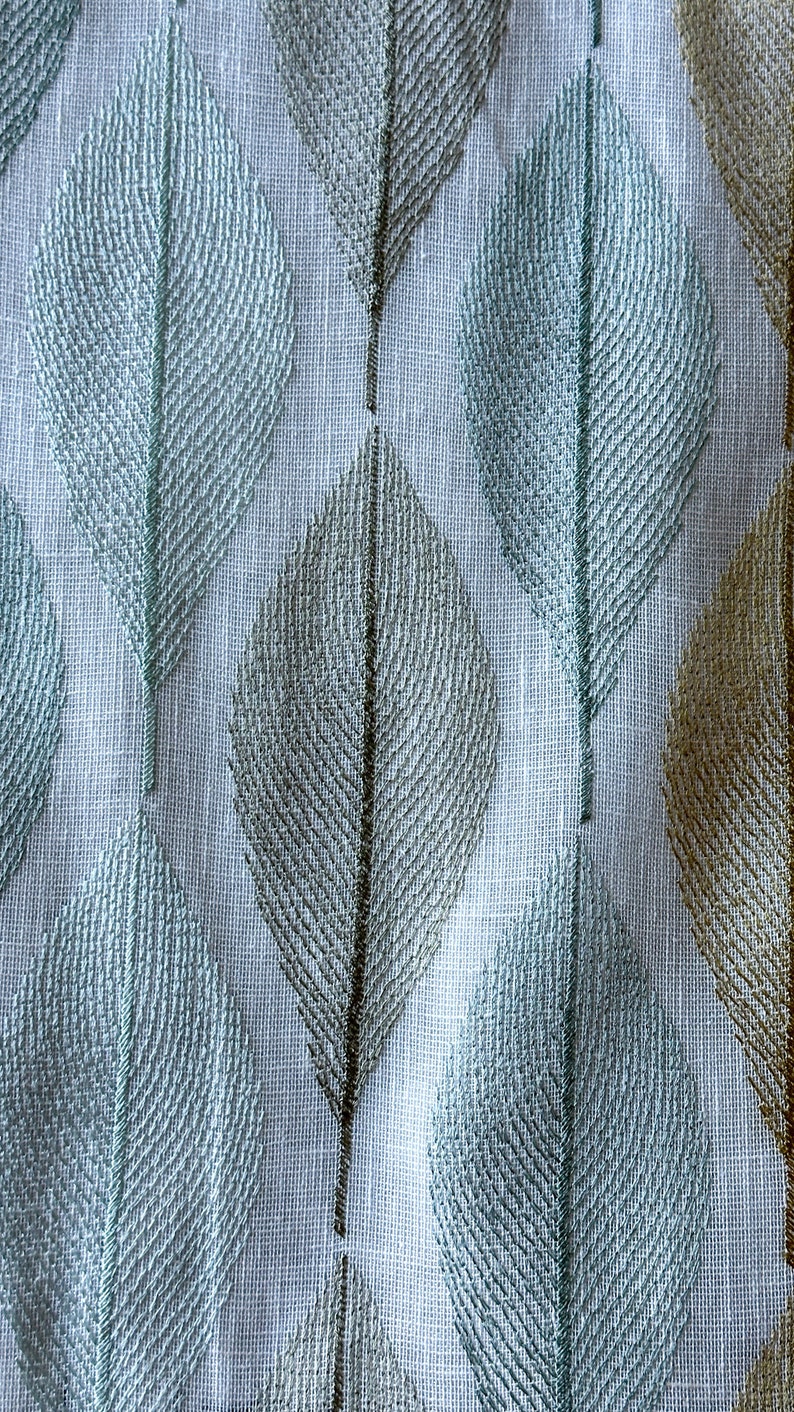 K&ouml;nnte beinhalten: Wei&szlig;er Stoff mit einem sich wiederholenden Muster aus blauen und braunen Bl&auml;ttern. Die Bl&auml;tter sind gestickt und haben eine strukturierte Optik.