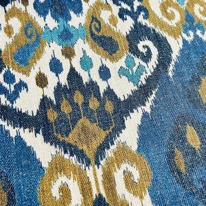 May include: Blue, white, and gold patterned fabric with an ikat design. The fabric has a woven texture.