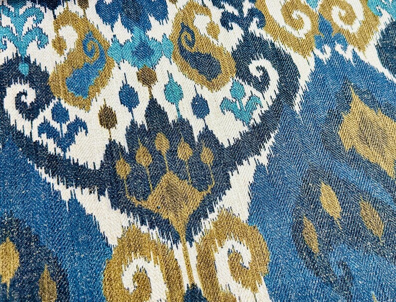 May include: Blue, white, and gold patterned fabric with an ikat design. The fabric has a woven texture.