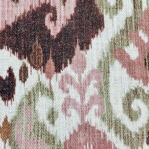 May include: Close-up of a woven fabric with an ikat pattern. The design features repeating abstract shapes in shades of brown, pink, and green on a white background. The fabric has a textured appearance.