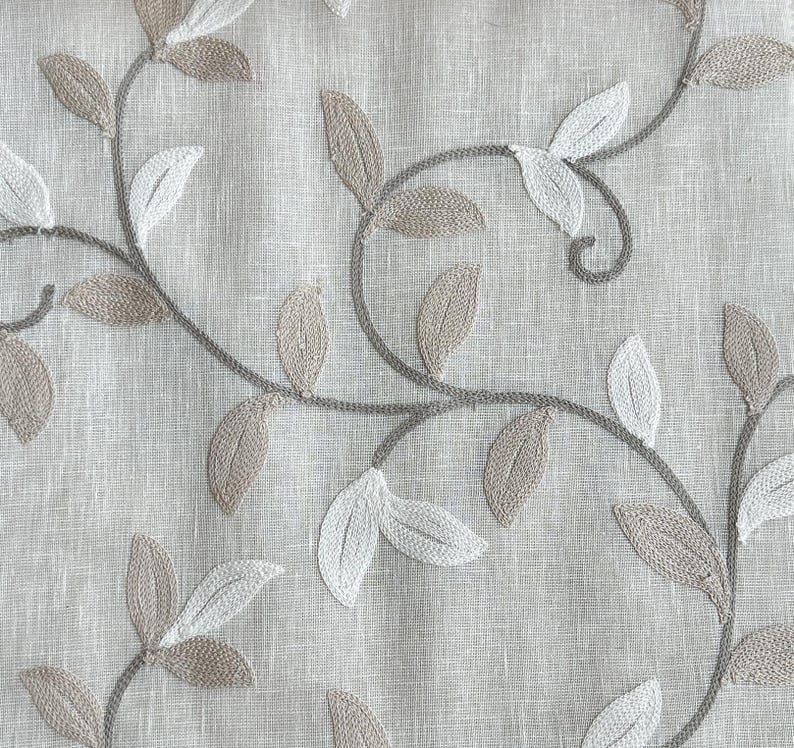 May include: A close-up of a beige fabric with an embroidered design of brown and white leaves and vines.