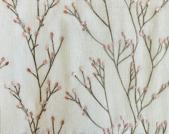 May include: A close-up of a white fabric with a delicate floral pattern embroidered in pink and green. The fabric has a subtle texture and a soft, natural look.