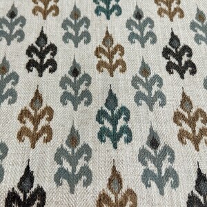 May include: A white fabric with a repeating pattern of stylized leaves in shades of brown, teal, and gray.